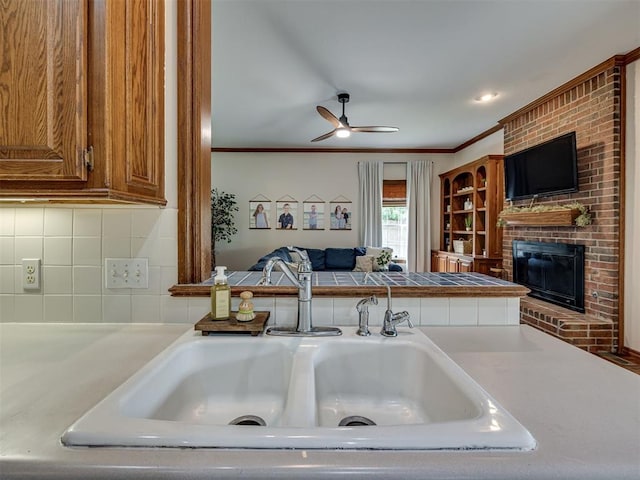 13925 Middleberry Rd, Edmond, OK 73013 - kitchen with a sink, a brick fireplace, a ceiling fan, decorative backsplash, and brown cabinetry