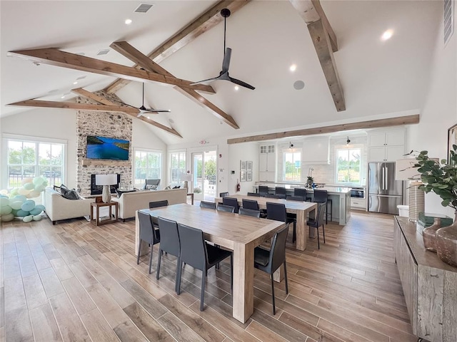 709 Montauk Way, Edmond, OK 73034 - dining space featuring a ceiling fan, high vaulted ceiling, beamed ceiling, light wood-type flooring, and a fireplace