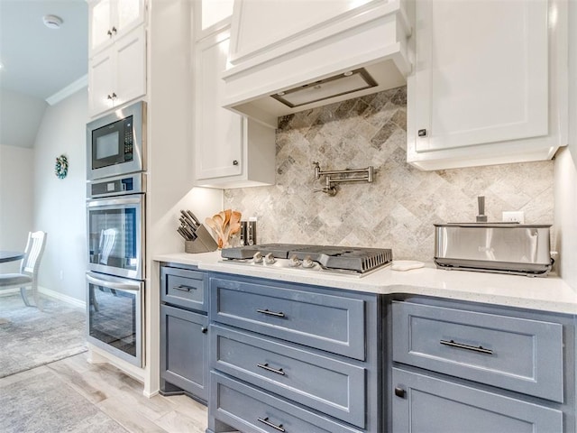 3317 Open Prairie Trl, Yukon, OK 73099 - kitchen featuring premium range hood, appliances with stainless steel finishes, white cabinetry, tasteful backsplash, and light wood-style floors