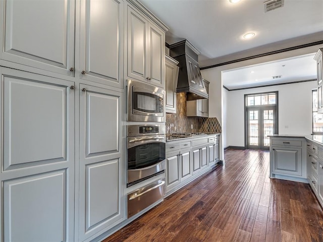 23 NE 3rd St, Oklahoma City, OK 73104 - kitchen featuring a warming drawer, stainless steel appliances, backsplash, dark wood finished floors, and custom range hood