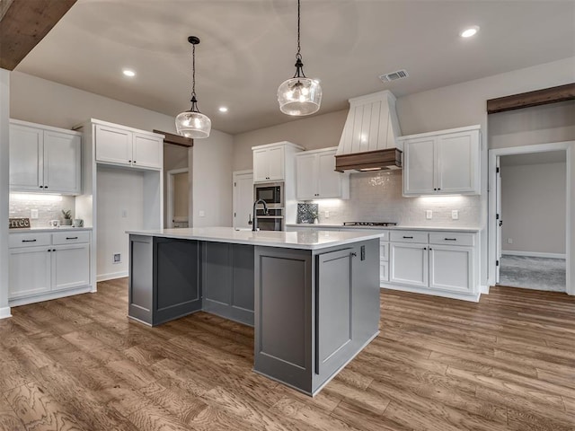 915 Kings Canyon Rd, Norman, OK 73071 - kitchen featuring premium range hood, white cabinetry, backsplash, wood finished floors, and cooktop
