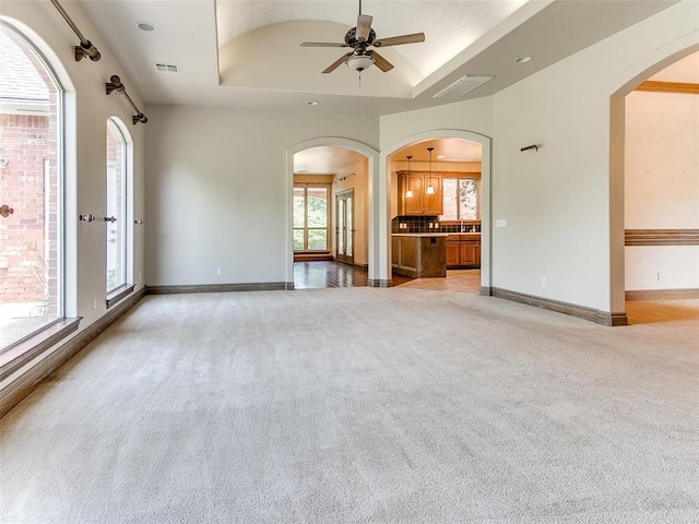 1031 Hidden Valley Ln, Choctaw, OK 73020 - unfurnished living room featuring arched walkways, light colored carpet, ceiling fan, and a raised ceiling