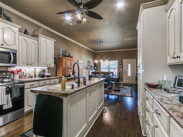 913 E Harrison Ave, Guthrie, OK 73044 - kitchen with appliances with stainless steel finishes, a ceiling fan, dark wood finished floors, an island with sink, and ornamental molding