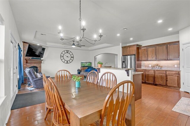13640 Ridge View Ln, Edmond, OK 73025 - dining room featuring a tray ceiling, a brick fireplace, a ceiling fan, light wood-style flooring, and recessed lighting