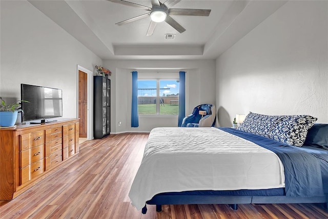13640 Ridge View Ln, Edmond, OK 73025 - bedroom featuring a raised ceiling, light wood-type flooring, and a ceiling fan