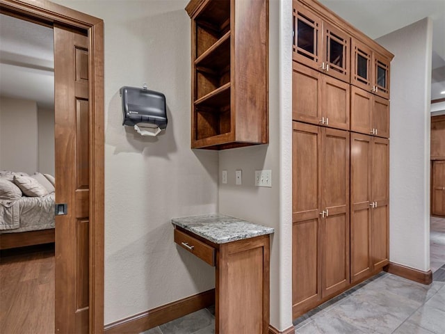 2120 Turtle Creek Dr, Norman, OK 73071 - kitchen with open shelves, brown cabinets, light stone counters, baseboards, and glass insert cabinets