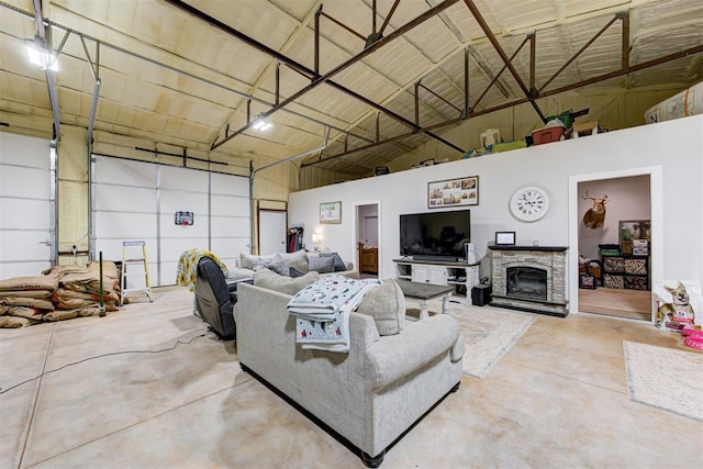 living area featuring concrete floors, high vaulted ceiling, a garage, and a fireplace