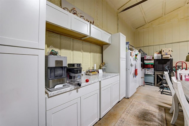 kitchen featuring vaulted ceiling, light countertops, white cabinets, freestanding refrigerator, and concrete floors