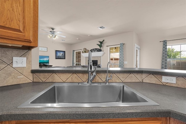 1204 Sheryl Ln, Altus, OK 73521 - kitchen view of a sink, dark countertops, decorative backsplash, a ceiling fan, and brown cabinetry