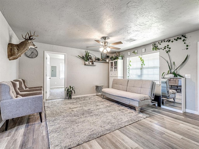 621 W 2nd St, Calumet, OK 73014 - living room featuring a textured ceiling, baseboards, electric panel, wood finished floors, and a ceiling fan