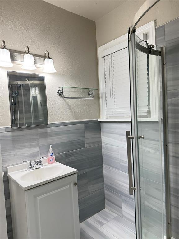 3117 NW 23rd St, Oklahoma City, OK 73107 - bathroom featuring a textured wall, tile walls, vanity, and a wainscoted wall
