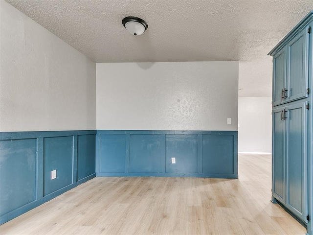 2713 SW 75th St, Oklahoma City, OK 73159 - unfurnished room featuring light wood-type flooring, a textured ceiling, a decorative wall, and a wainscoted wall