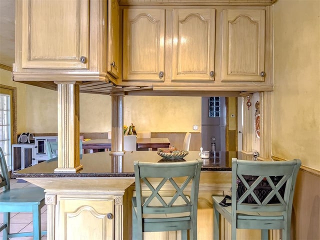 1117 SW 37th St, Oklahoma City, OK 73109 - kitchen with decorative columns, a kitchen breakfast bar, dark countertops, and light brown cabinets