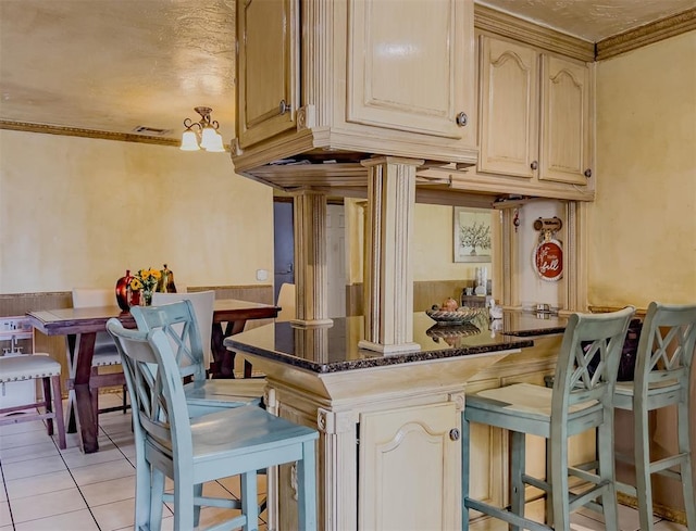 1117 SW 37th St, Oklahoma City, OK 73109 - kitchen featuring a kitchen bar, dark stone counters, light tile patterned flooring, ornamental molding, and a peninsula
