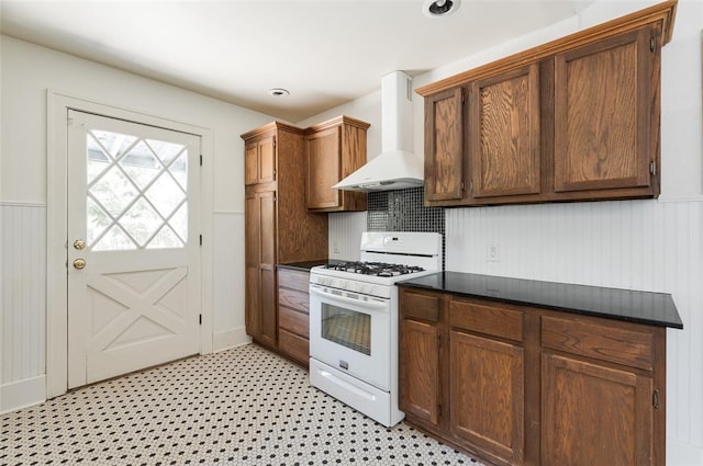 1505 NW 34th St, Oklahoma City, OK 73118 - kitchen featuring wall chimney range hood, white gas range oven, dark countertops, a wainscoted wall, and light flooring
