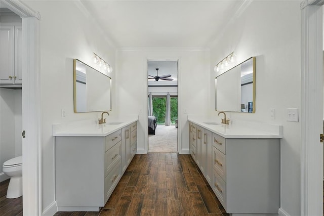 2108 Woodhill Rd, Edmond, OK 73025 - bathroom with hardwood / wood-style flooring, two vanities, toilet, a ceiling fan, and ornamental molding