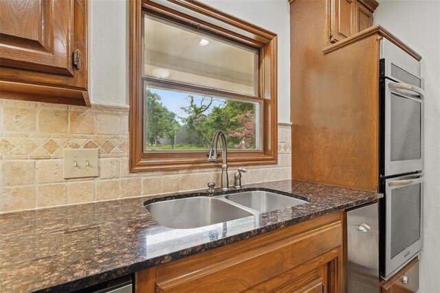 2108 Woodhill Rd, Edmond, OK 73025 - kitchen with a sink, brown cabinetry, backsplash, stainless steel double oven, and dark stone counters