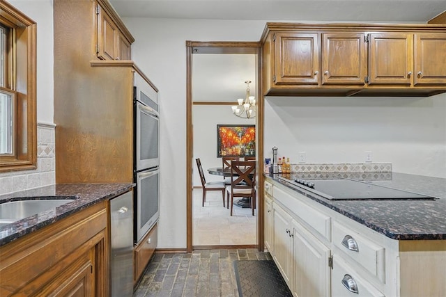 2108 Woodhill Rd, Edmond, OK 73025 - kitchen featuring stainless steel appliances, a chandelier, brown cabinets, and dark stone countertops