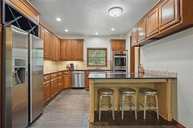 2108 Woodhill Rd, Edmond, OK 73025 - kitchen featuring stainless steel appliances, a sink, a peninsula, tasteful backsplash, and brown cabinets