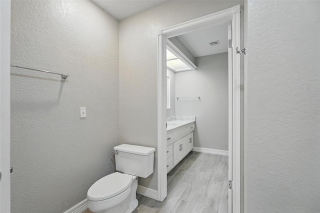 2108 Woodhill Rd, Edmond, OK 73025 - bathroom featuring vanity, toilet, a textured wall, wood finished floors, and baseboards