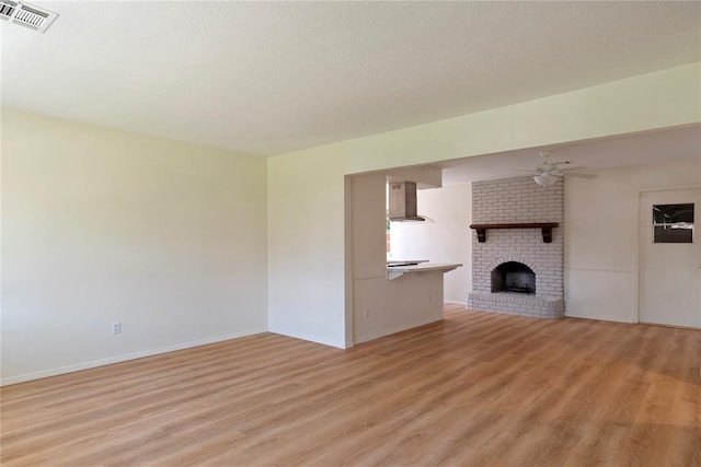 1121 NW 105th St, Oklahoma City, OK 73114 - unfurnished living room with light wood-style flooring, a ceiling fan, a fireplace, and a textured ceiling