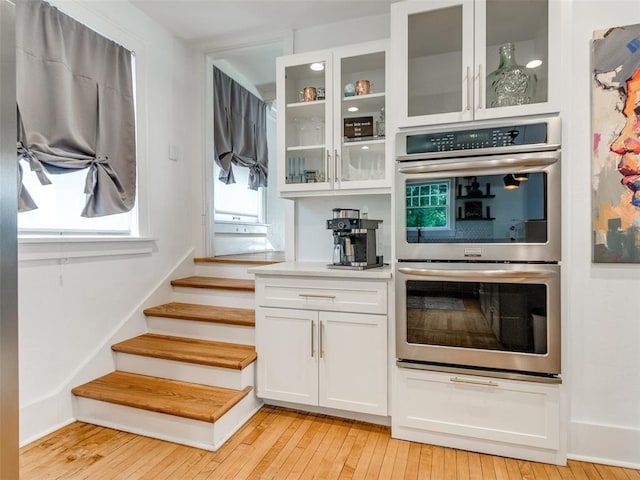 1218 NW 21st St, Oklahoma City, OK 73106 - kitchen with double oven, light wood-style floors, white cabinetry, glass insert cabinets, and light countertops