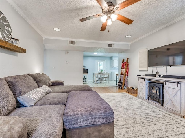 332 Crest Ln, Noble, OK 73068 - living area featuring a textured ceiling, light wood-type flooring, ceiling fan, crown molding, and a wood stove