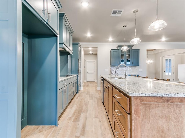 12825 Painted Sky, Edmond, OK 73007 - kitchen with a sink, glass insert cabinets, light stone counters, light wood-type flooring, and an island with sink