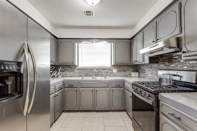 601 Woodland Way, Oklahoma City, OK 73127 - kitchen with stainless steel appliances, under cabinet range hood, gray cabinets, tasteful backsplash, and a textured ceiling