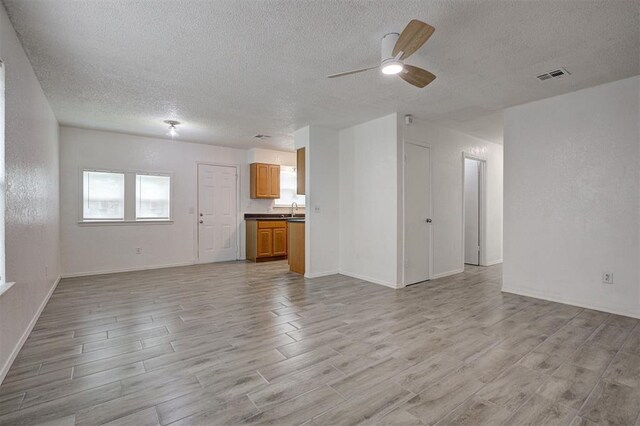 1633 SE 52nd St, Oklahoma City, OK 73129 - unfurnished living room with a textured ceiling, light wood-style flooring, a sink, a ceiling fan, and baseboards