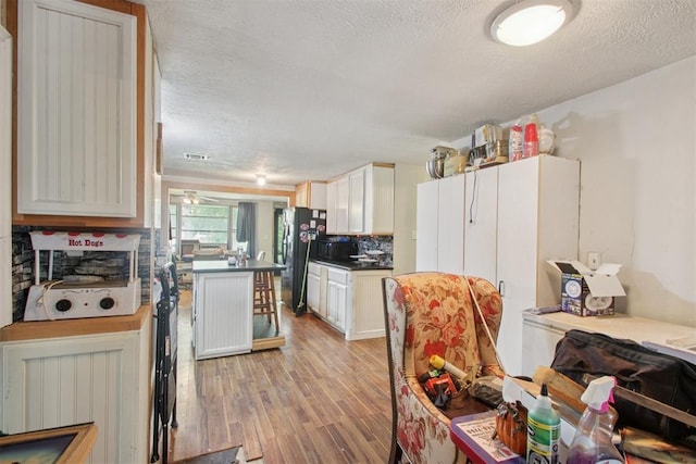 1001 N Pine St, Midwest City, OK 73130 - kitchen with light wood-type flooring, freestanding refrigerator, dark countertops, a textured ceiling, and white cabinets
