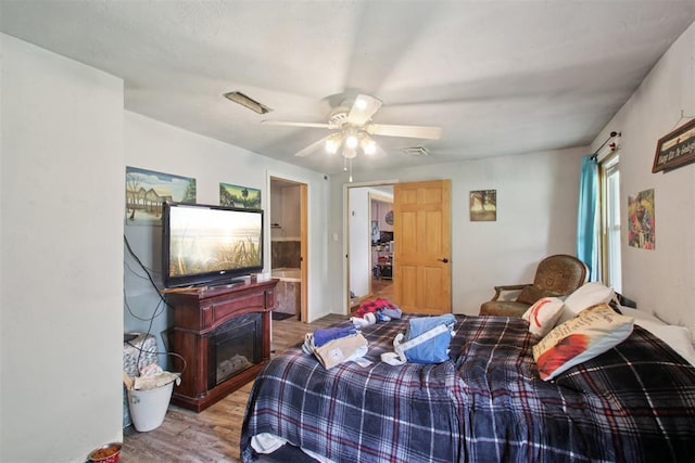 1001 N Pine St, Midwest City, OK 73130 - bedroom with wood finished floors, a ceiling fan, a glass covered fireplace, and connected bathroom