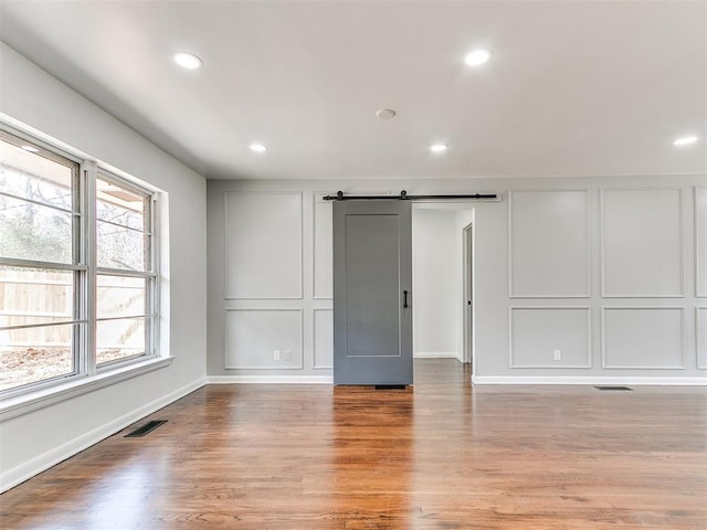 1224 W Brooks St, Norman, OK 73069 - unfurnished bedroom with a decorative wall, wood finished floors, recessed lighting, a barn door, and baseboards