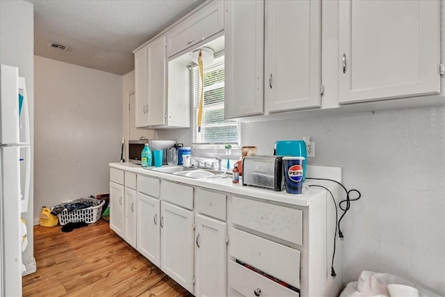 2119 Pearson Dr, Midwest City, OK 73110 - kitchen with freestanding refrigerator, white cabinets, light countertops, a textured ceiling, and light wood-style floors