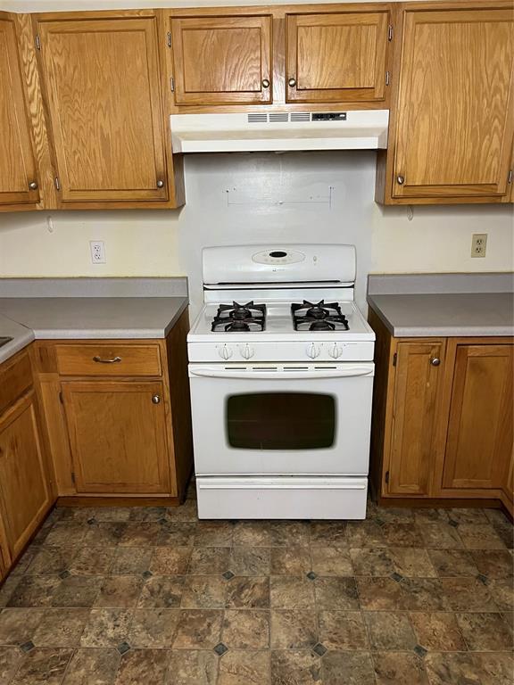 1012 Box St, Altus, OK 73521 - kitchen featuring white range with gas stovetop, under cabinet range hood, brown cabinetry, and stone finish floors
