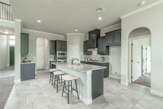 1417 Cordgrass Ct, Edmond, OK 73013 - kitchen with a sink, appliances with stainless steel finishes, arched walkways, tasteful backsplash, and a kitchen island with sink