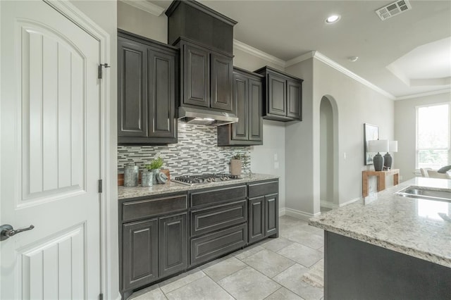 1417 Cordgrass Ct, Edmond, OK 73013 - kitchen with stainless steel gas stovetop, under cabinet range hood, decorative backsplash, arched walkways, and light stone countertops