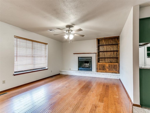 16687 SE 16th St, Choctaw, OK 73020 - unfurnished living room with ceiling fan, a textured ceiling, a brick fireplace, built in features, and light wood-style flooring