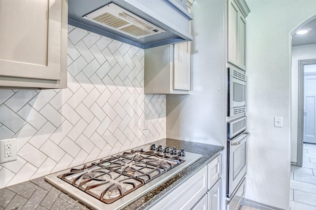 3024 Wakefield Rd, Edmond, OK 73034 - kitchen with appliances with stainless steel finishes, range hood, arched walkways, backsplash, and dark stone counters