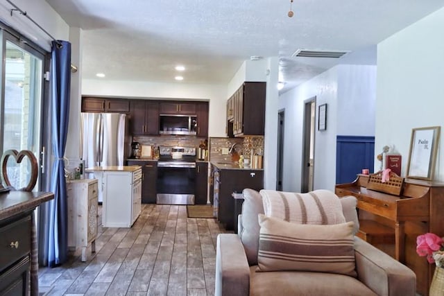 5704 N Warren Ave, Oklahoma City, OK 73112 - kitchen with stainless steel appliances, a kitchen island, open floor plan, dark brown cabinetry, and tasteful backsplash