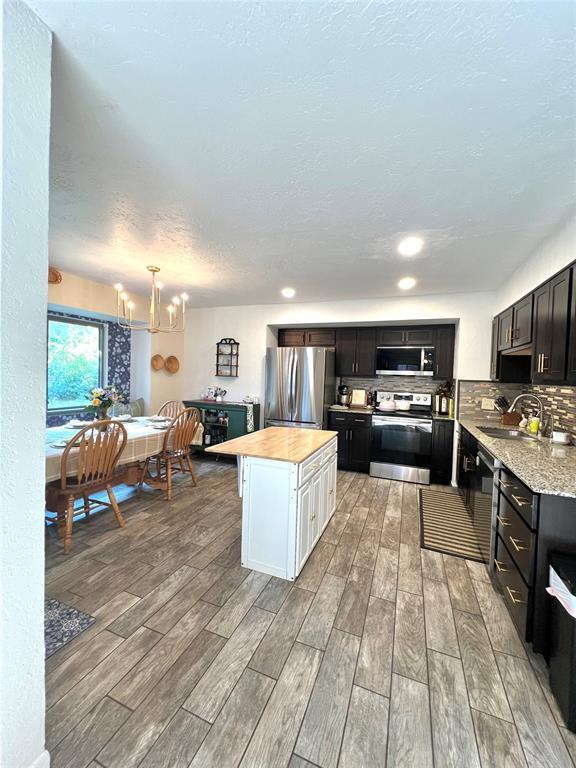 5704 N Warren Ave, Oklahoma City, OK 73112 - kitchen with stainless steel appliances, light wood-type flooring, a center island, a chandelier, and decorative backsplash