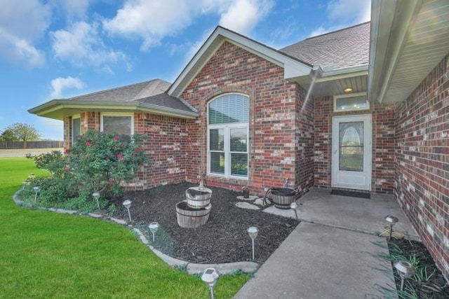 2 NW Havenshire Cir, Lawton, OK 73505 - view of exterior entry featuring brick siding, a lawn, a shingled roof, and a patio