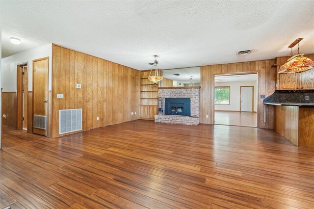 1317 S 58th St, Duncan, OK 73534 - unfurnished living room with wood-type flooring, wood walls, a textured ceiling, and a brick fireplace