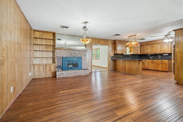 1317 S 58th St, Duncan, OK 73534 - unfurnished living room featuring a textured ceiling, wooden walls, wood finished floors, ceiling fan, and a brick fireplace