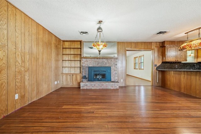 1317 S 58th St, Duncan, OK 73534 - unfurnished living room with wood finished floors, wooden walls, a textured ceiling, a brick fireplace, and a sink