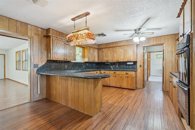 1317 S 58th St, Duncan, OK 73534 - kitchen with a peninsula, brown cabinetry, tasteful backsplash, light wood-type flooring, and wooden walls