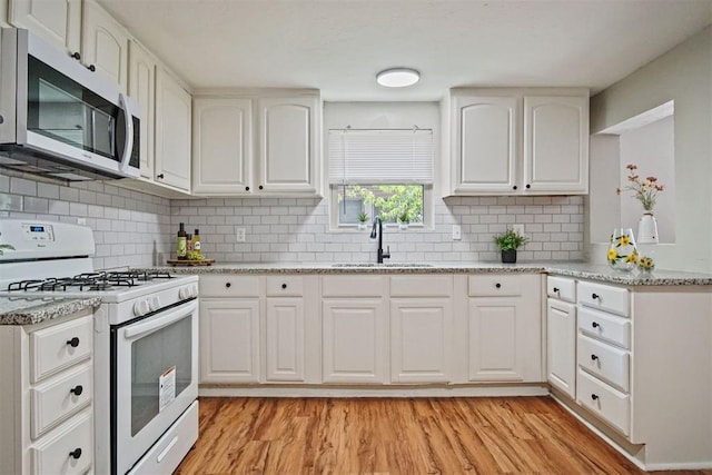 940 NE 32nd St, Oklahoma City, OK 73105 - kitchen with white gas stove, stainless steel microwave, light wood-style floors, white cabinets, and light stone countertops
