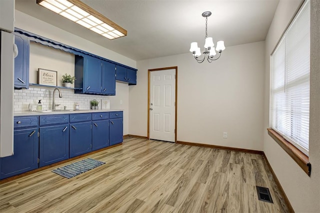 520 SE 47th St, Oklahoma City, OK 73129 - kitchen with blue cabinetry, a sink, light countertops, a chandelier, and light wood-style flooring