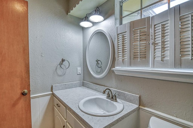 1439 Greenbriar Dr, Norman, OK 73072 - half bath with vanity, toilet, a textured wall, and wainscoting