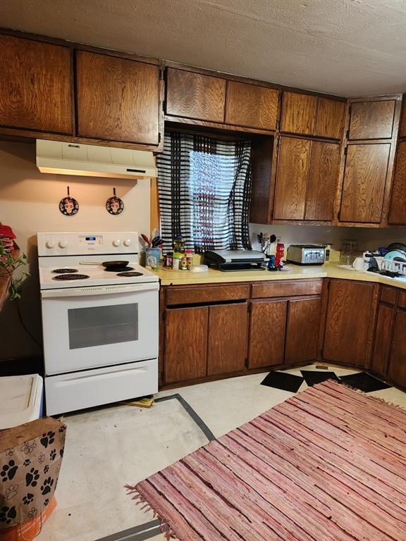 310 Mcgee St, Eufaula, OK 74432 - kitchen with white electric stove, under cabinet range hood, light countertops, light flooring, and a textured ceiling